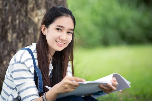 Sonriendo hermosa chica asiática leyendo libro y trabajando en el árbol en — Foto de Stock