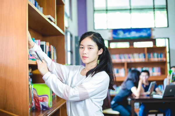 Aziatische vrouwelijke studenten houden voor selectie boeken in bibliotheek — Stockfoto