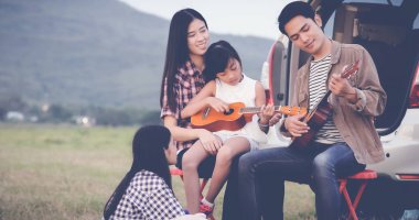 Asya aile t oturmuş ukulele oynamaktan mutlu küçük kız