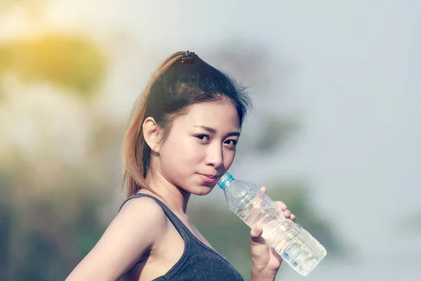 Sportlich frau asien holding und trinkwasser outdoor auf sonnigem da — Stockfoto