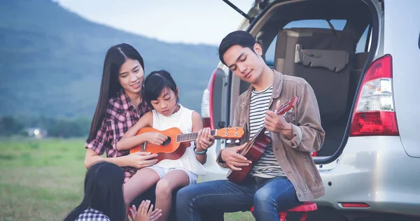 Feliz niña jugando ukelele con asiático familia sentado en t —  Fotos de Stock