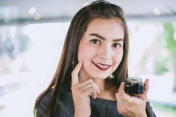 Uma bela mulher asiática usando um produto de cuidados da pele, hidratante o — Fotografia de Stock