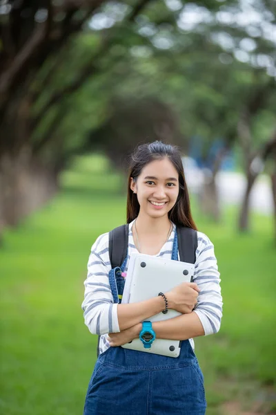 Красивая азиатская студентка держит книги и улыбается в камеру — стоковое фото