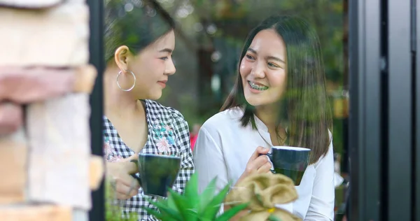 Две азиатки пьют кофе и веселые женщины сплетничают — стоковое фото