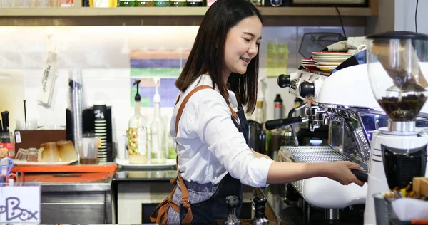 Азіатські жінки Barista посміхається і за допомогою кавомашину в s кави — стокове фото