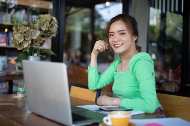 Asyalı iş kadınları gülümsüyor ve notları analiz belgeleri ve grafik finansal diyagramı için kullanıyor ve kahve dükkanında kahve içiyor.