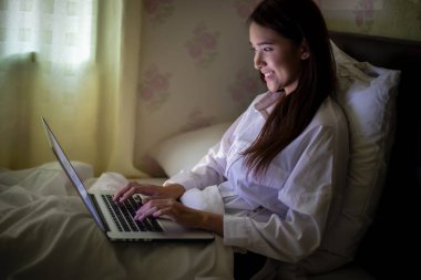 Asyalı kadın geceleri çalışmak için defter kullanıyor. Gülümsüyor ve evde çalışmaktan hoşlanıyor..