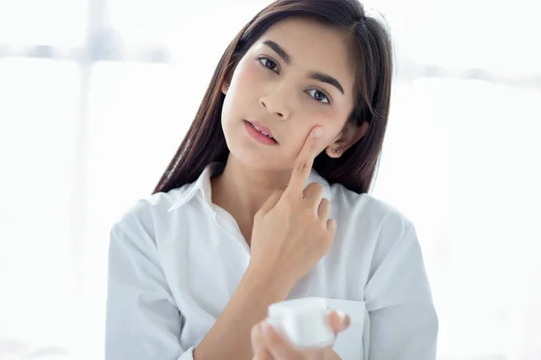 A beautiful woman asian using a skin care product, moisturizer or lotion taking care of her dry complexion. Moisturizing cream in female hands .