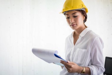 Asyalı kadın mühendisler denetliyor, çalışıyor ve ofiste planları tutuyor.