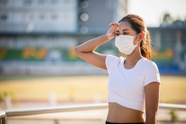 Genç Asyalı fitness sporcusu yoruluyor ve şehrin tozunu ve kirliliğini korumak için maske takıyor.