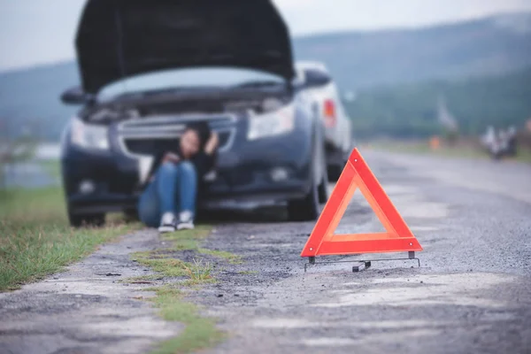 Asian woman sitting on floor near broken down car with Red triangle of a car on the road