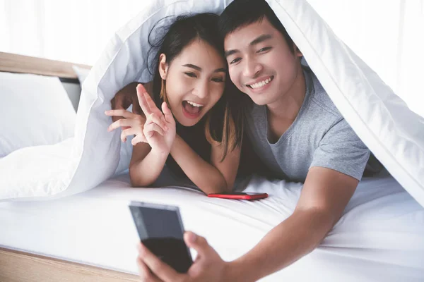 Asyalı Çift Aşıklar Cep Telefonlarıyla Oynuyorlar Evde Yatakta Selfie Çekiyorlar — Stok fotoğraf