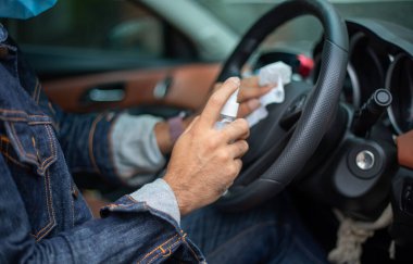 Koronavirüs koruması için arabayı temizlemek için sprey alkol kullanan Asyalı bir adam.