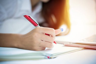 Asyalı bir kadın not defterine not yazmak için kalem kullanıyor ve evdeki yatağında çalışmak için bir defter kullanıyor..