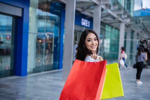 衣料品店に立ちながら笑顔で買い物袋を持つ美しいアジアの若い女性 消費主義 人々は続ける — ストック写真