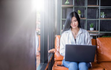 Asyalı iş kadınları evde çalışmak için dizüstü bilgisayar kullanıyorlar. Gülümsüyor ve çalışmaktan hoşlanıyor..