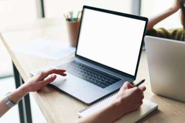 Womans hands using laptop and writing in notepad