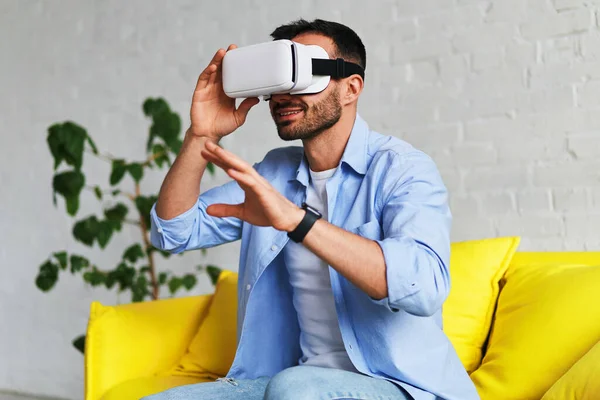 Excited man in blue shirt wearing virtual reality glasses touching something and smiling while having VR experience — Stockfoto