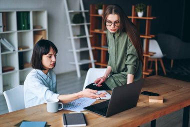 Two serious businesswomen having a meeting using laptop in minimalist office