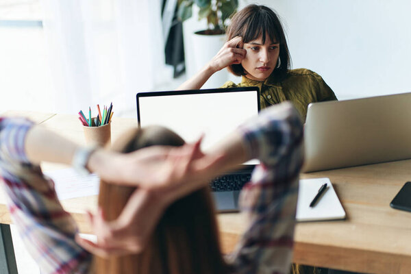 Back view of two young woman working in modern office using laptop