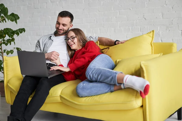 Jong schattig paar op zoek naar laptop scherm gelegen op de gele bank — Stockfoto