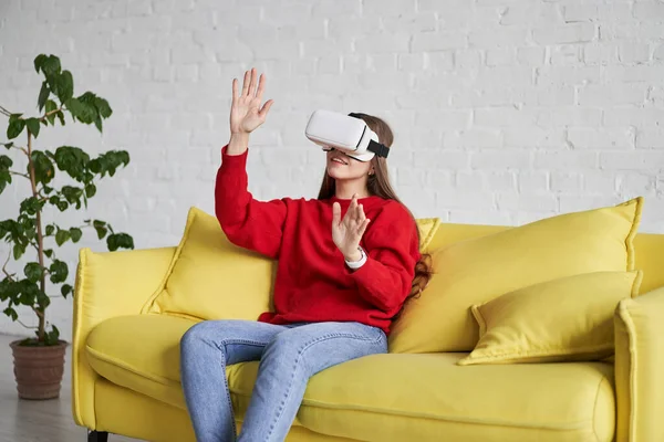 Opgewonden vrouw in rode trui met virtual reality bril die iets aanraakt en glimlacht terwijl ze VR-ervaring heeft — Stockfoto