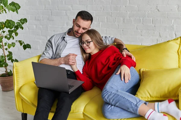 Jong schattig paar op zoek naar laptop scherm gelegen op de gele bank — Stockfoto