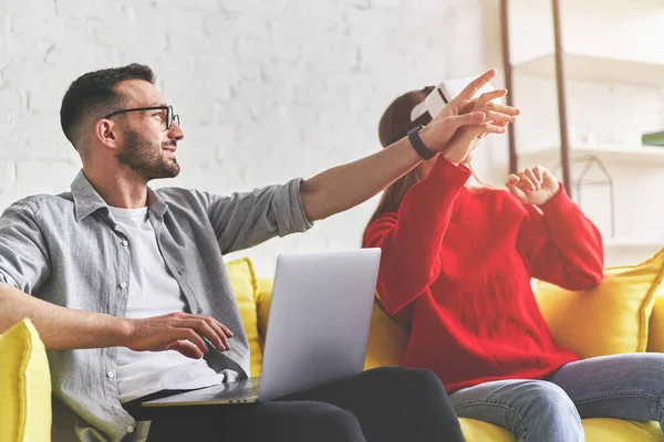 Jong glimlachend paar in VR bril spelen video game met laptop op gele bank — Stockfoto