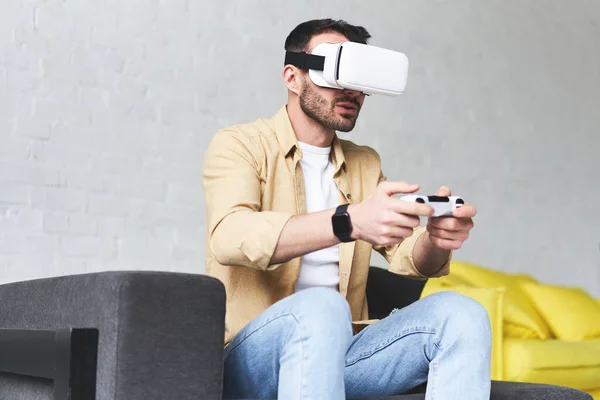 Portret van verbaasd opgewonden man kijkend naar virtual reality glazen met joystick in zijn hand — Stockfoto
