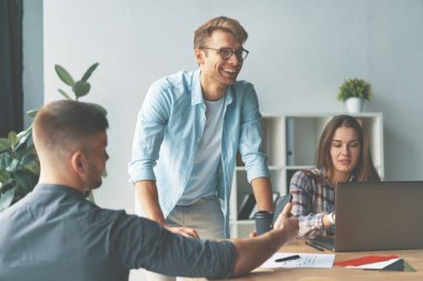 İki erkek ve kadın, işyerinde otururken birlikte çalışıyorlar.