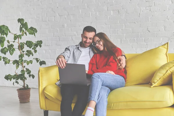 Paar zittend op de gele bank. Man toont film op laptop. — Stockfoto