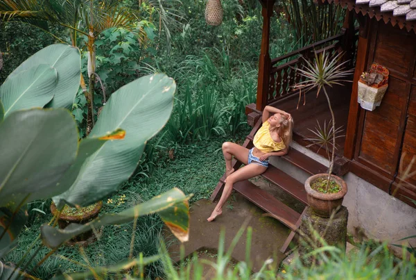 Ormanın yanındaki tropikal balkonda oturan kot şortlu kadın. Stok Fotoğraf