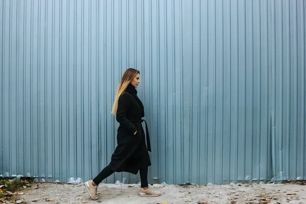 Mooie jonge vrouw in casual kleding lopen tegen het hek — Stockfoto