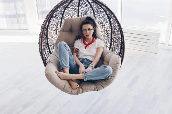Beautiful young woman sitting in suspension cane chair — Stock Photo, Image