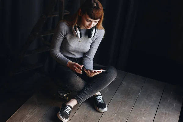 Niña sentada en monopatín con auriculares y tableta — Foto de Stock