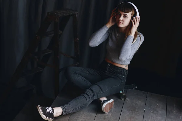 Young girl sitting on skateboard with headphones — Stock Photo, Image