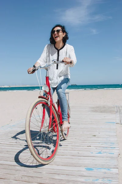 Mujer joven y feliz montando en bicicleta en una playa —  Fotos de Stock