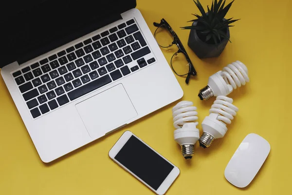 Energisparande glödlampor, telefon och laptop på gula — Stockfoto