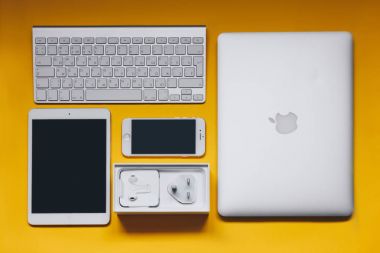Sarı arka plan üzerinde klavye, iphone 7, şarj cihazı, ipad ve Macbook Üstten Görünüm