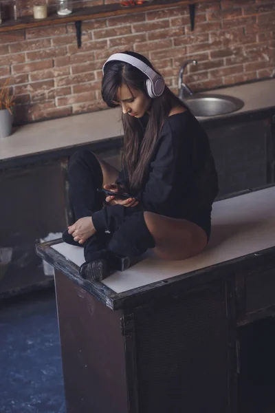 Mujer joven con auriculares sentada en la mesa de la cocina — Foto de Stock