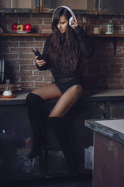 Mujer joven con auriculares sentada en la mesa de la cocina — Foto de Stock