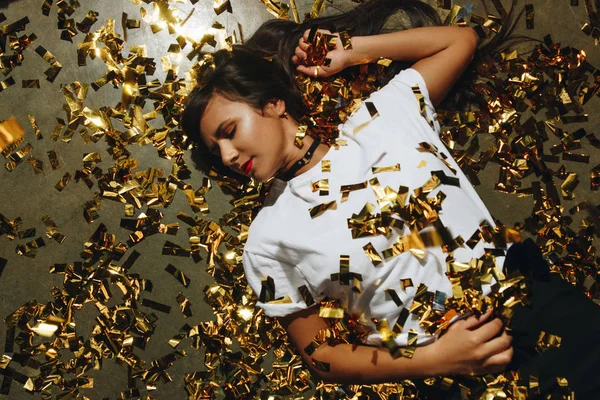 Mujer en el suelo con confeti dorado — Foto de Stock