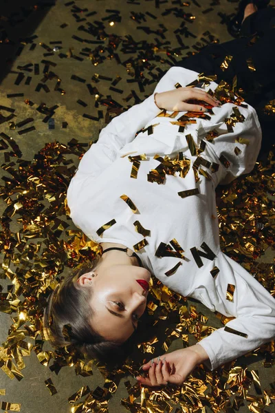 Mujer en el suelo con confeti dorado — Foto de Stock