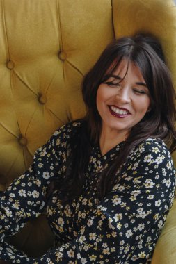 Sarı koltukta oturan gülümseyen genç kadın.