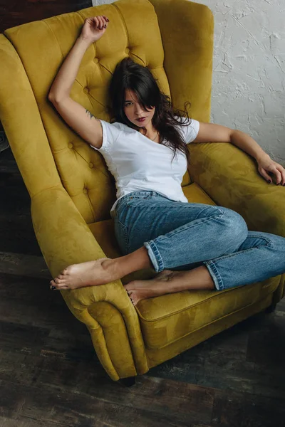 Beautiful young woman sitting in yellow armchair — Stock Photo, Image