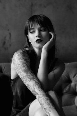 Küçük siyah elbiseli güzel bir kadın sandalyede oturuyor.