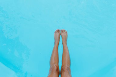Yüzme havuzunun mavi suyunda genç bir kadının bacakları.