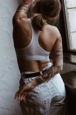 Dövmeli, pamuklu sutyen ve beyaz kot pantolon giyen kadın.