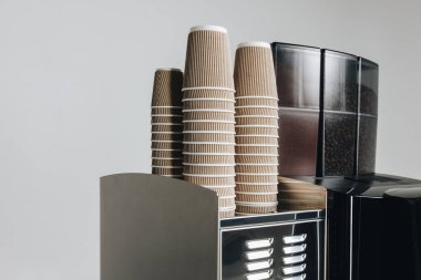 Yanında kağıt bardaklar olan kahve makinesi. Kahveyi götür.