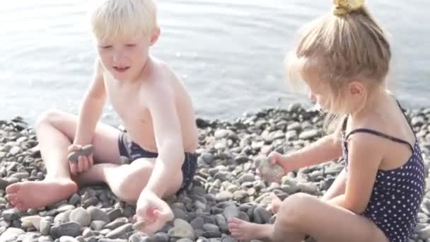 Ein blonder Junge mit einem kleinen Mädchen wirft Mädchen ins Meer — Stockvideo